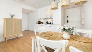 Una cucina moderna con mobili bianchi, un tavolo da pranzo in legno con sottopiatti intrecciati e lampade a sospensione in vimini.