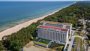 Un grande albergo con tetto piatto, situato vicino a una spiaggia e circondato da alberi fitti.
