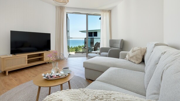 Un soggiorno moderno con una televisione a schermo piatto, un divano, un tavolino da caffè e un balcone con vista sul mare.