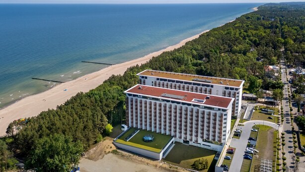 A large hotel with a flat roof, located near a beach and surrounded by dense forest. - Large Apartment With sea View, Indoor Pool (Rewal)