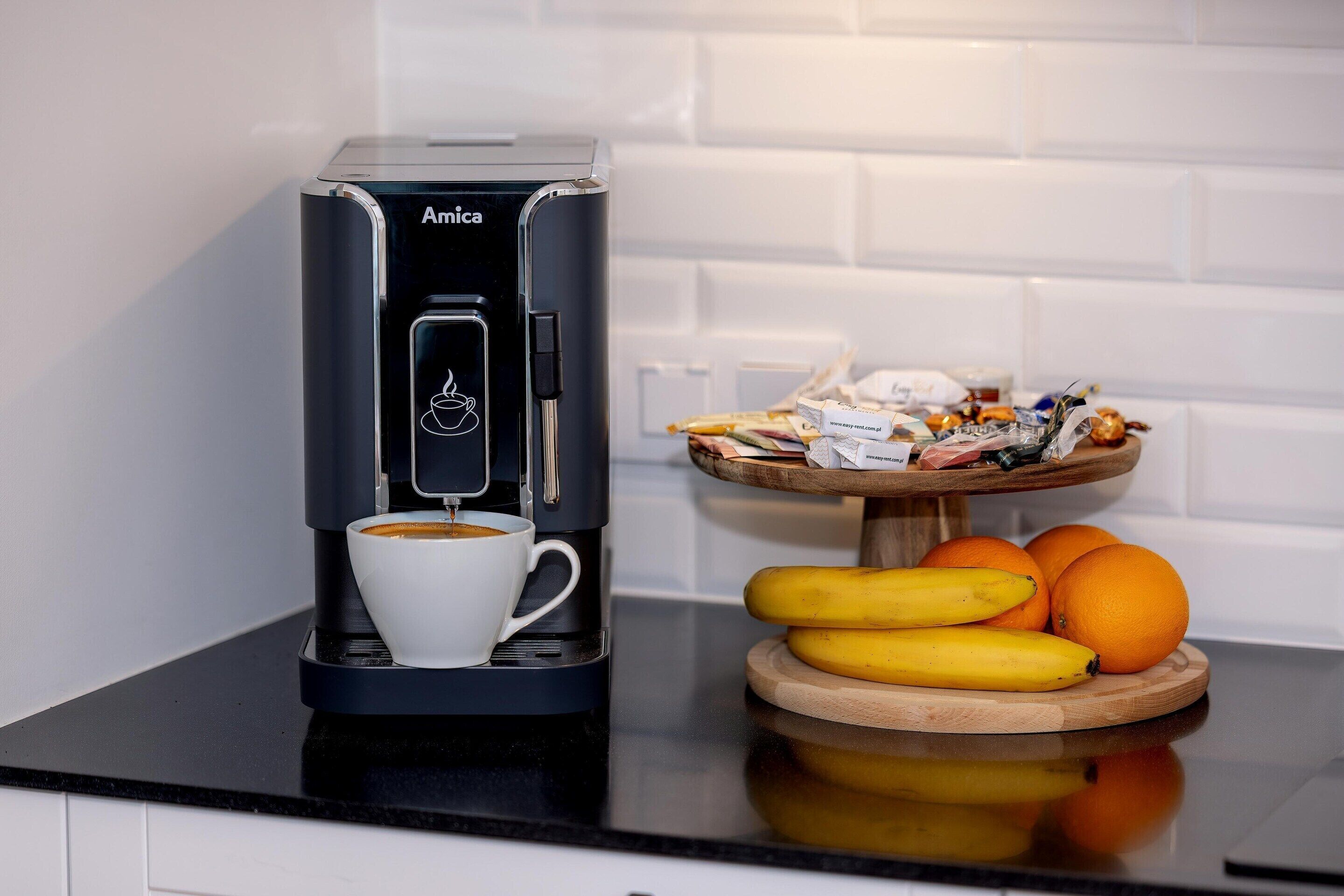 A coffee maker with a cup of coffee, bananas, and oranges on a kitchen counter.