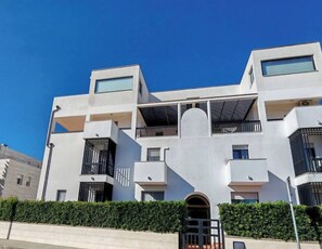 A modern multi-story building with balconies, a central entrance, and a clear sky. - Mediterranean life style, sea view, 10 min. walk from city centre. (Alghero)