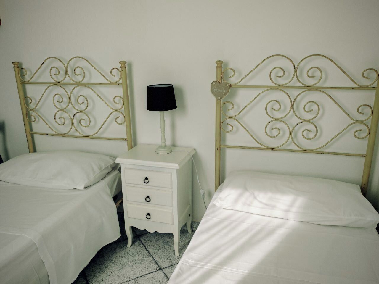 Een slaapkamer met twee eenpersoonsbedden, een nachtkastje met lamp en een klein dressoir.