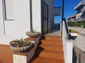 A corridor with a tiled floor, two planters with plants, a metal gate, and a staircase leading to an upper level. - Mediterranean life style, sea view, 10 min. walk from city centre. (Alghero)