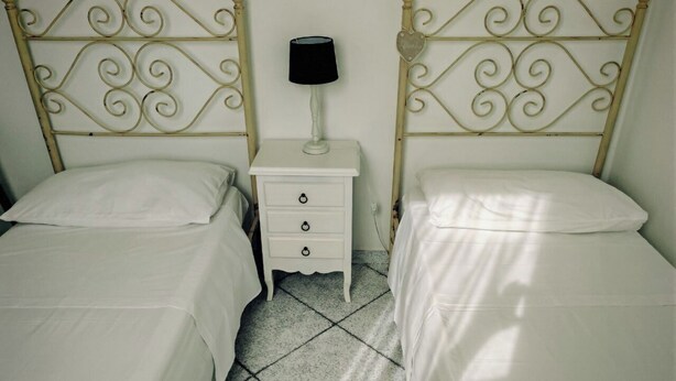 Quarto com duas camas de solteiro, uma mesa de cabeceira com abajur e piso de azulejos.