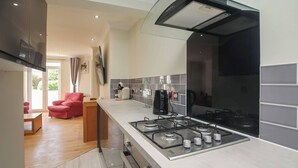A modern kitchen with a gas stove, a coffee maker, and a red chair in the adjacent living area. - Charming Central Kingston Flat by the River (Kingston Upon Thames)