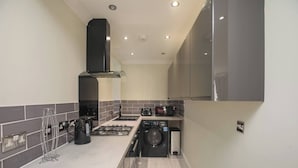 A compact kitchen with a gas stove, a built-in washing machine, and a microwave. - Charming Central Kingston Flat by the River (Kingston Upon Thames)