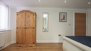 A bedroom with a wooden wardrobe, a bed, a mirror, and a framed picture on the wall. - Charming Central Kingston Flat by the River (Kingston Upon Thames)