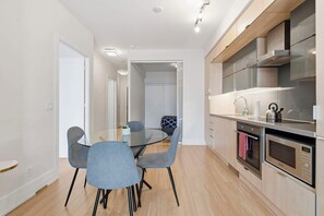 A modern kitchen with stainless steel appliances, a dining area with a glass table and chairs, and a hallway leading to a bedroom. - Cityscape Haven 2BR with Fantastic CN Tower View (Toronto)