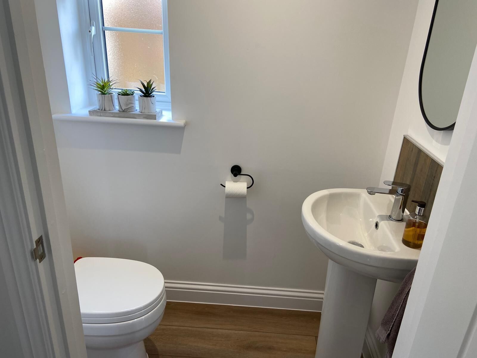 A small bathroom with a toilet, a sink, and a window with plants.
