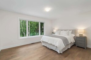 Une chambre avec une grande fenêtre, un lit, une table de chevet et une lampe fixée au mur.