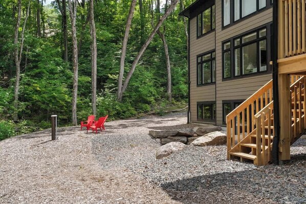 A modern building with a wooden staircase and a gravel area with red chairs.