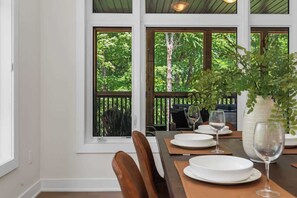 Un coin repas avec une table dressée pour deux personnes, de grandes fenêtres et une vue sur les arbres.