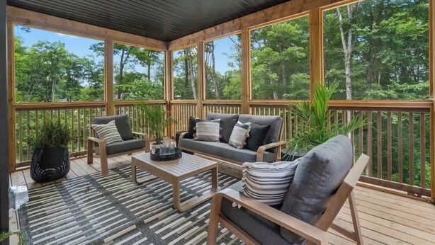 Un espace extérieur aménagé, abrité et doté de mobilier en bois et de grandes fenêtres.