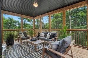 A covered outdoor seating area with wooden furniture and large windows.