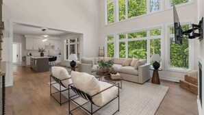 Un vaste espace de vie avec une grande fenêtre, une cuisine à l’arrière-plan et un coin salon avec une table basse et des fauteuils.