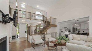 Un vaste espace de vie comprenant un escalier, une cheminée et, au fond, une cuisine moderne.