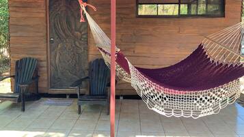 A hammock hanging between two poles, wooden chairs, a door with a decorative panel, and a window with a ceiling fan.