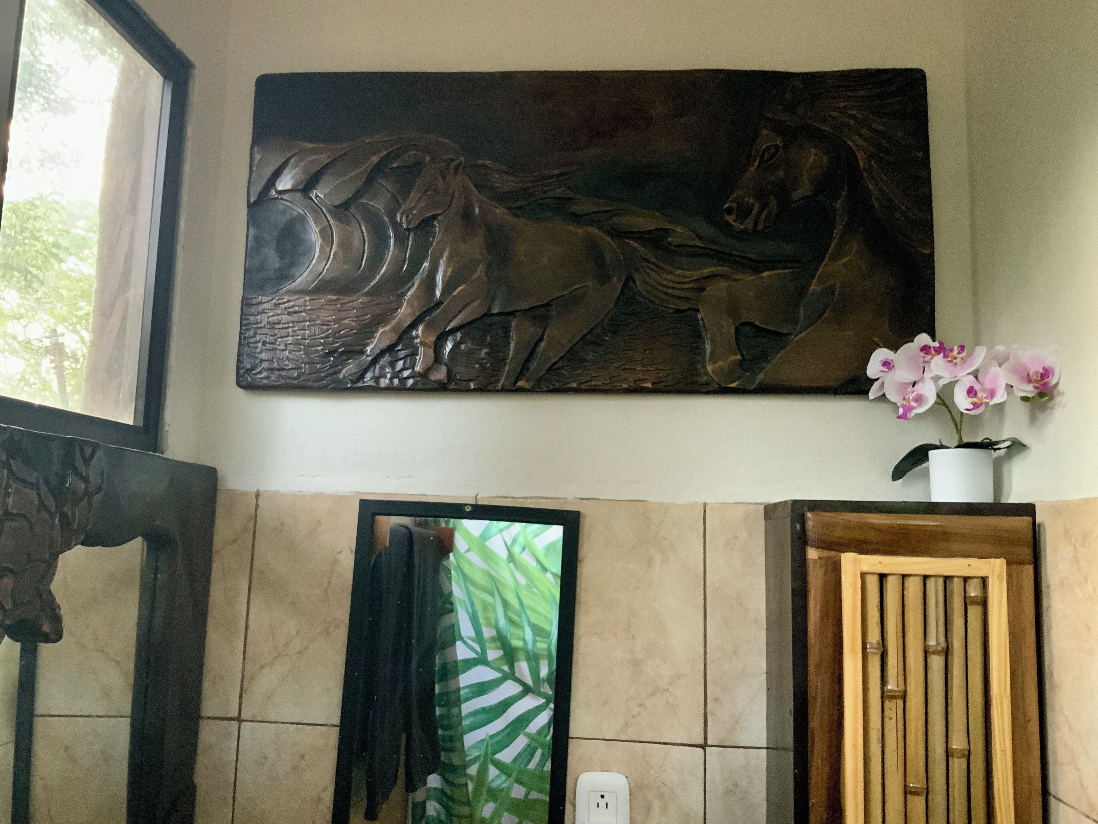 Een badkamer met een groot, aan de muur bevestigd beeld van paarden, een spiegel, een potorkidee en een houten deur.