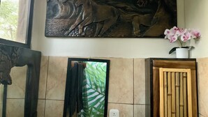 A bathroom with a large wall-mounted sculpture of horses, a mirror, a potted orchid, and a wooden door. - Playa Avellanas Hand-Carved Casita Walk to Beach Private Jungle Stay (Playa Avellanas)