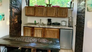 A compact kitchen with wooden cabinets, a marble countertop, a sink, a coffee maker, and a slow cooker. - Playa Avellanas Hand-Carved Casita Walk to Beach Private Jungle Stay (Playa Avellanas)