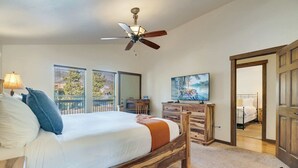 Ein Schlafzimmer mit einem hölzernen Bett, einem Deckenventilator, einem Fernseher und Blick ins Freie durch große Fenster.