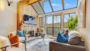 Ein gemütliches Wohnzimmer mit Kamin, bequemen Sitzmöglichkeiten und einem großen Fenster mit Blick ins Freie.