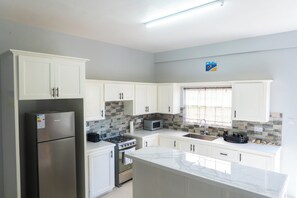 Eine moderne Küche mit weißen Schränken, einem Edelstahl-Kühlschrank, einem Gasherd und einer Mikrowelle.