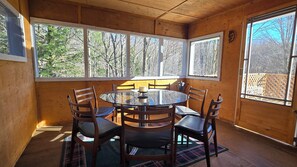 A wooden cabin interior with a round table and six chairs, large windows, and a view of trees. - 2 Acre Nature Retreat, Private Lake, Firepit, Bird Sanctuary, Stargazing (Wentworth)