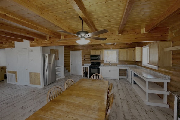 A log cabin interior with a dining area, kitchen, and a ceiling fan.