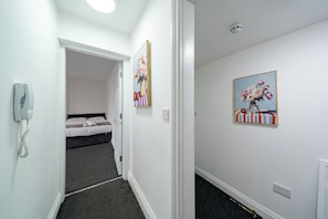 A hallway with a bed in the background, a phone on the wall, and two paintings. - Modern Family Flat | Sleeps 6 (Ilkeston)