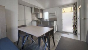 A modern kitchen with a dining table and chairs, a built-in oven, and a window providing natural light. - 3-bedroom mobile home near the ocean + pool (Saint-Georges-de-Didonne)