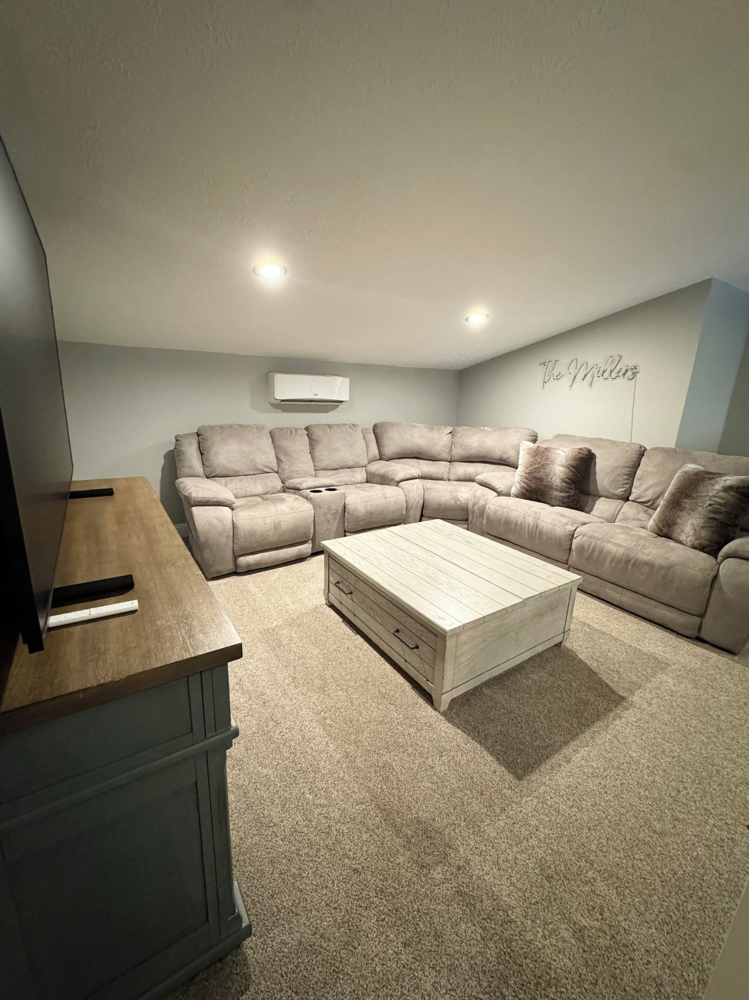 A living room with a sectional sofa, a wooden coffee table, and a TV stand.