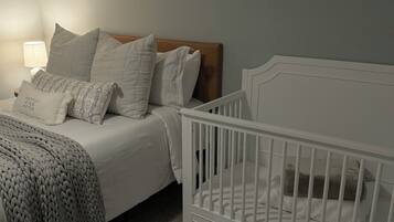 A bedroom with a bed, a crib, a lamp, and a textured throw blanket.