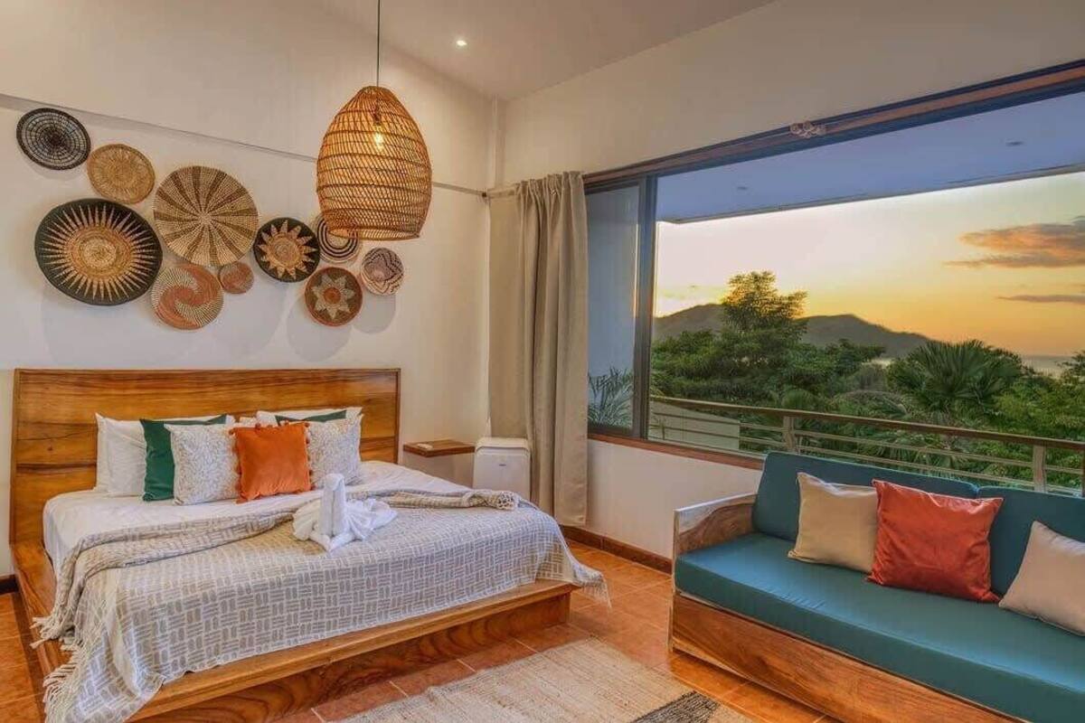 A bedroom with a large bed, a sofa, and a view of the outdoors.