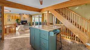 A spacious living area with a wooden staircase, a fireplace, and a kitchen island. - Maplewood Getaway | Sauna & Bar (Maplewood)