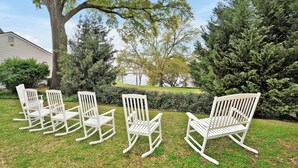 Une pelouse avec quatre chaises à bascule blanches et un grand arbre.