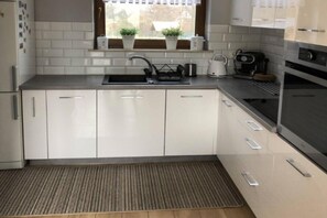 A modern kitchen with white cabinets, a stainless steel sink, and a built-in oven. - Holiday Home, Large Garden With Playground, Gazebo (Ustka)