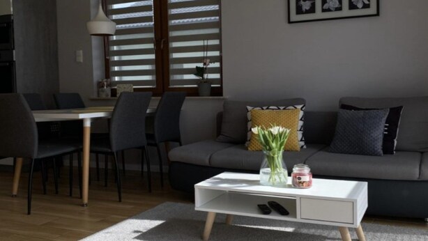 Ein modernes Wohnzimmer mit einem grauen Sofa, einem weißen Couchtisch und einem Essbereich mit Stühlen und einem Tisch.