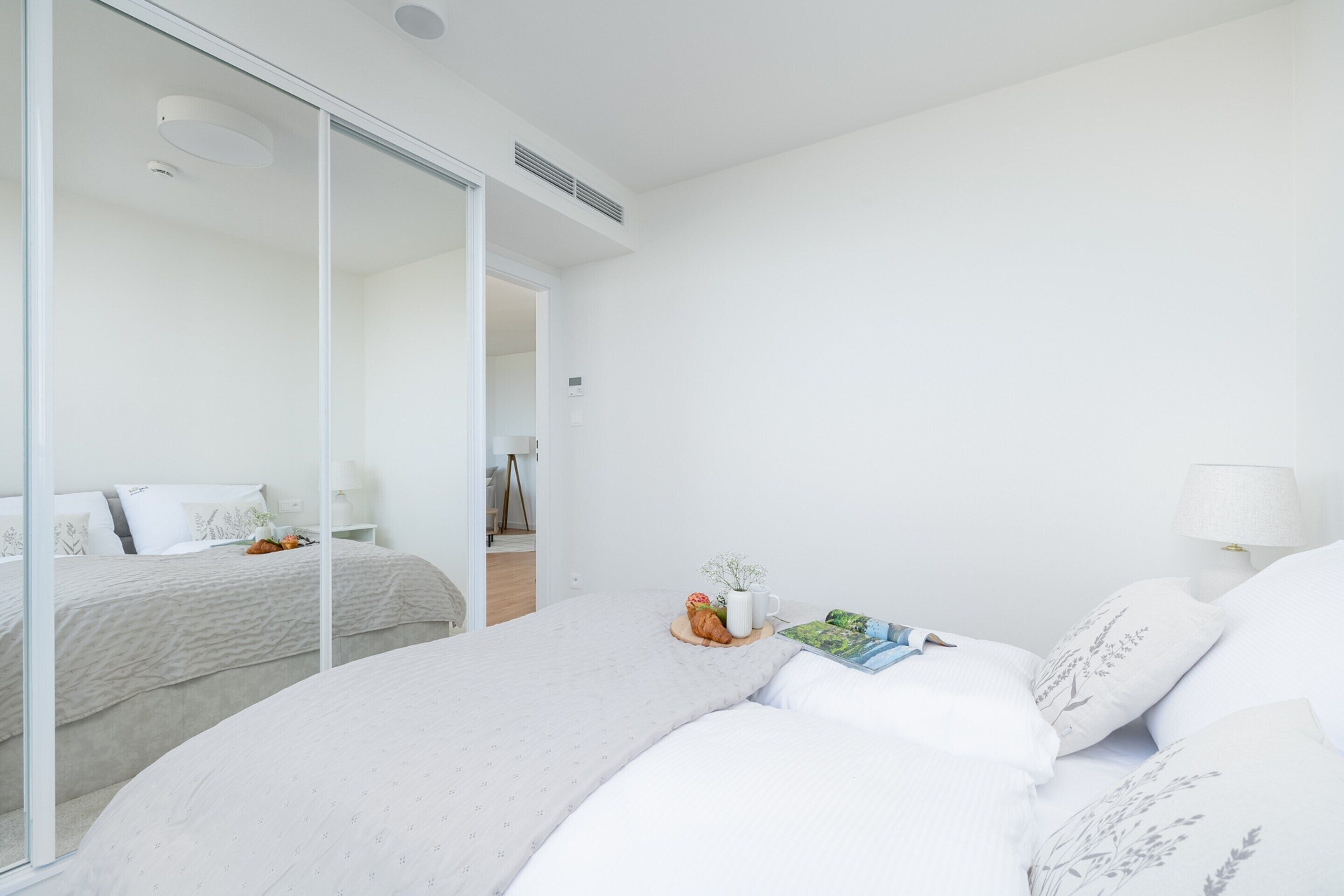 A modern bedroom with a large bed, a bedside table, a lamp, and a mirror.
