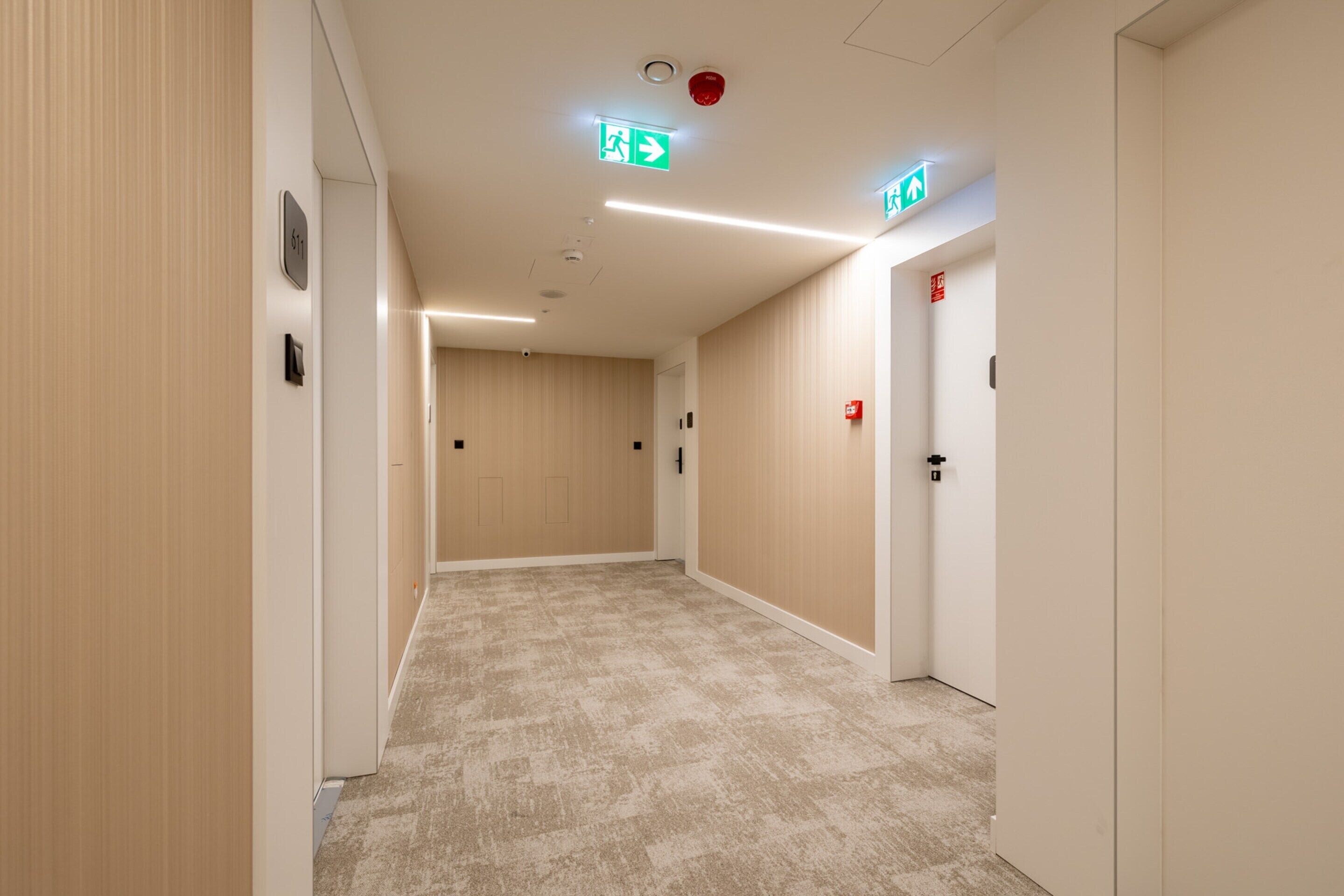 Ein Korridor mit beigem Teppich, Holzwandverkleidung und Türen mit Notausgangsschildern.