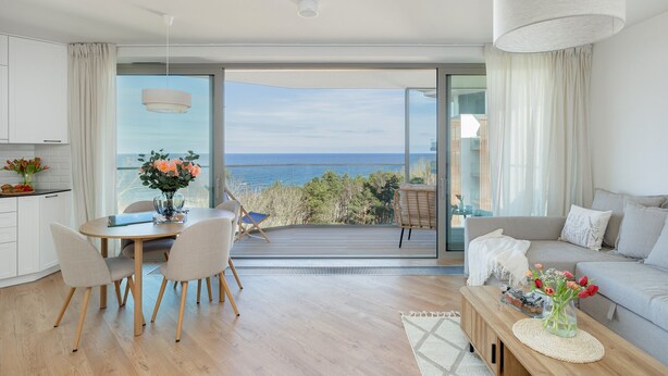 A modern living room with a balcony overlooking the sea, a dining area with a table and chairs, and a sofa with a view. - Stunning Seaview Retreat for 4 in Pobierowo (Rewal)