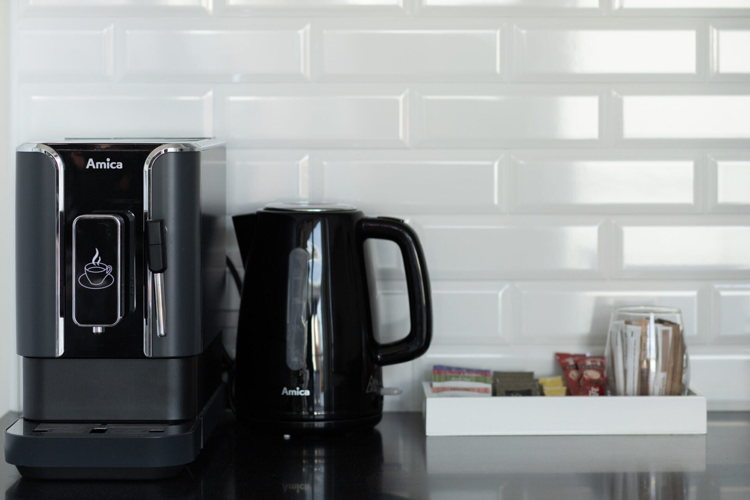A black coffee maker and a black mug on a kitchen counter with a white tiled backsplash.