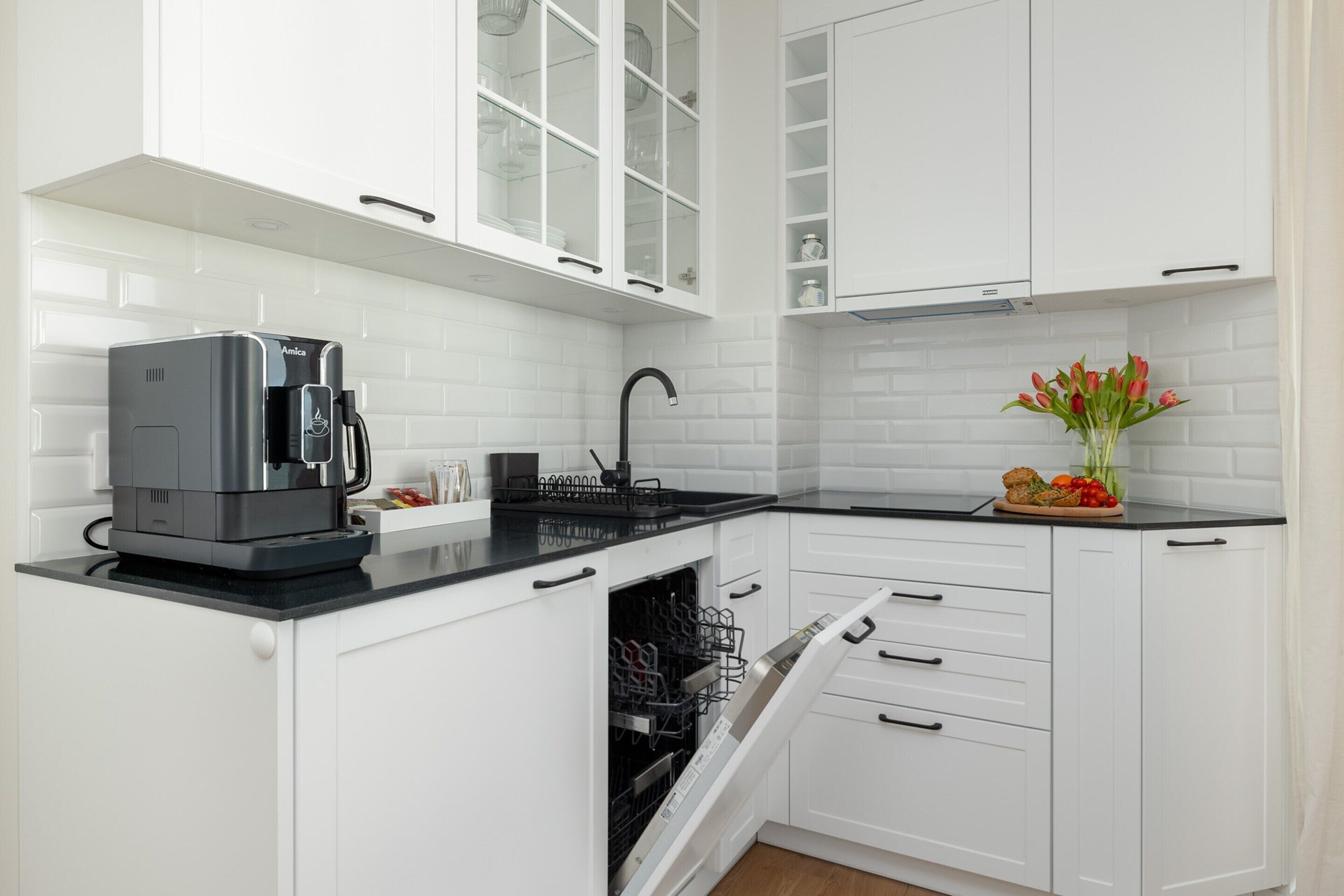 Uma cozinha moderna com armários brancos, bancada preta, cafeteira e um vaso com flores.