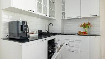 Uma cozinha moderna com armários brancos, bancada preta, cafeteira e um vaso com flores.