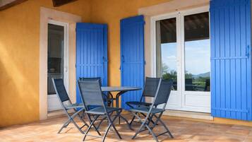 A patio with a table and four chairs, blue shutters, and a view of the outdoors.