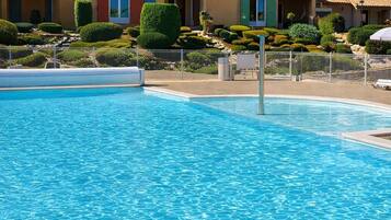 A swimming pool with a clear blue water surface, surrounded by a well-maintained garden with neatly trimmed bushes and a fence.