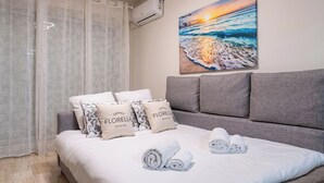 A bedroom with a bed, grey headboard, white bedding, and a painting of a sunset over the sea. - Le Roxane joli cocon avec petit terrasse (Cannes)