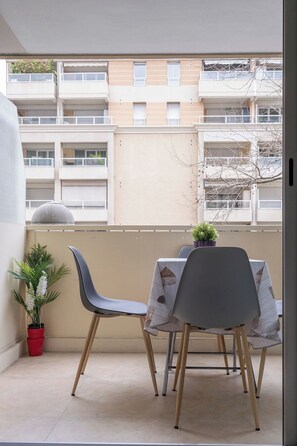 Un balcón con dos sillas, una mesa, una planta en maceta y vistas de un edificio de varios pisos.