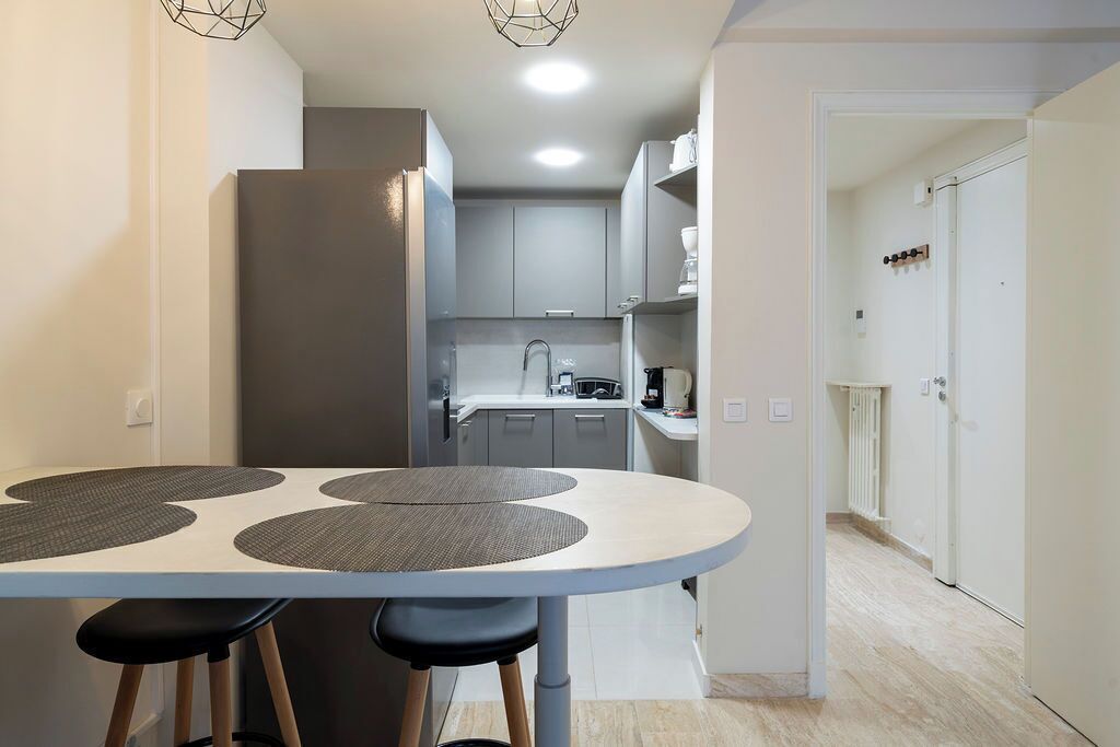 Una cocina moderna con armarios grises, una encimera blanca y una zona de comedor con una mesa redonda y taburetes.